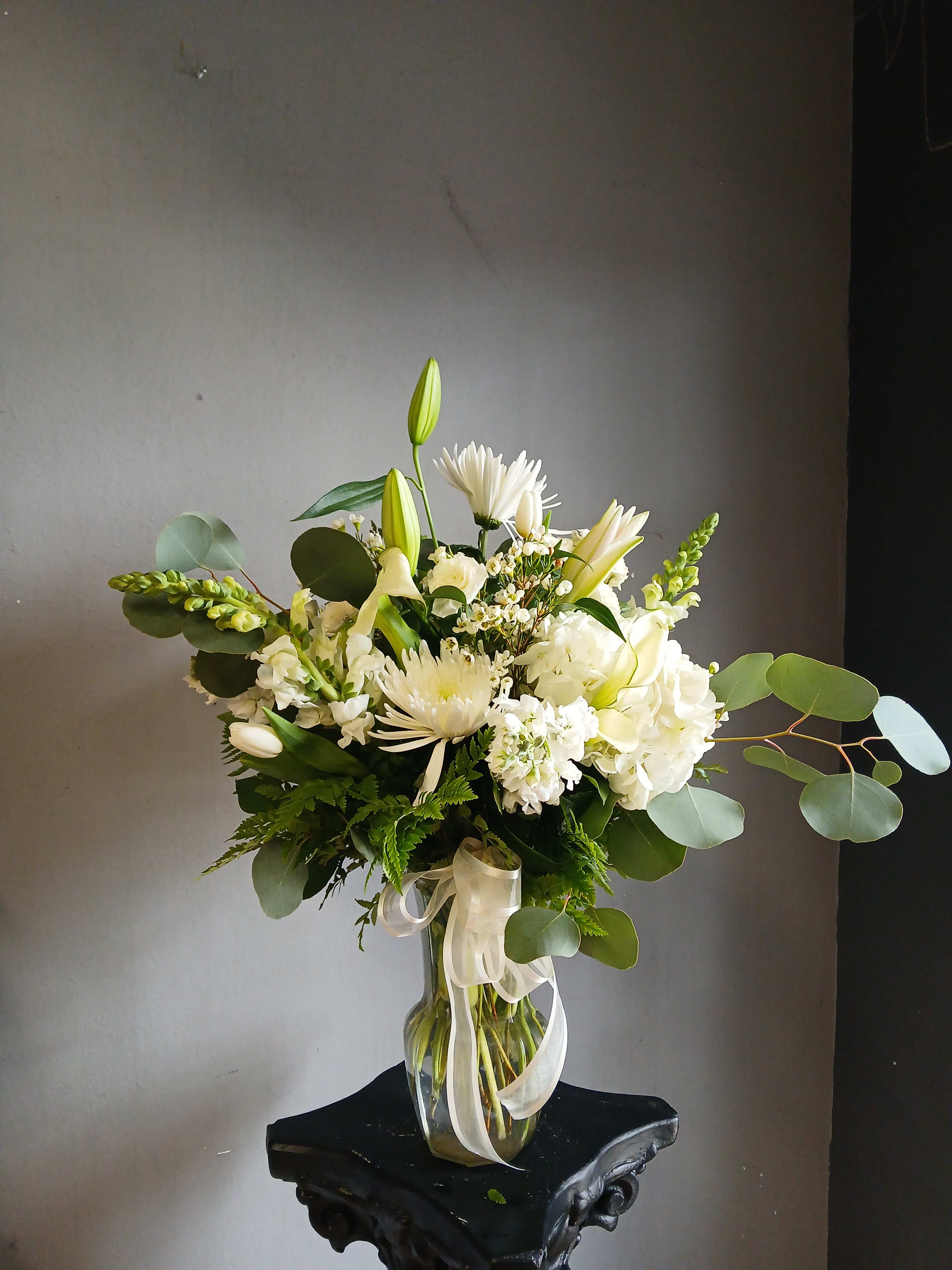 White floral arrangement in a clear glass vase with ribbon