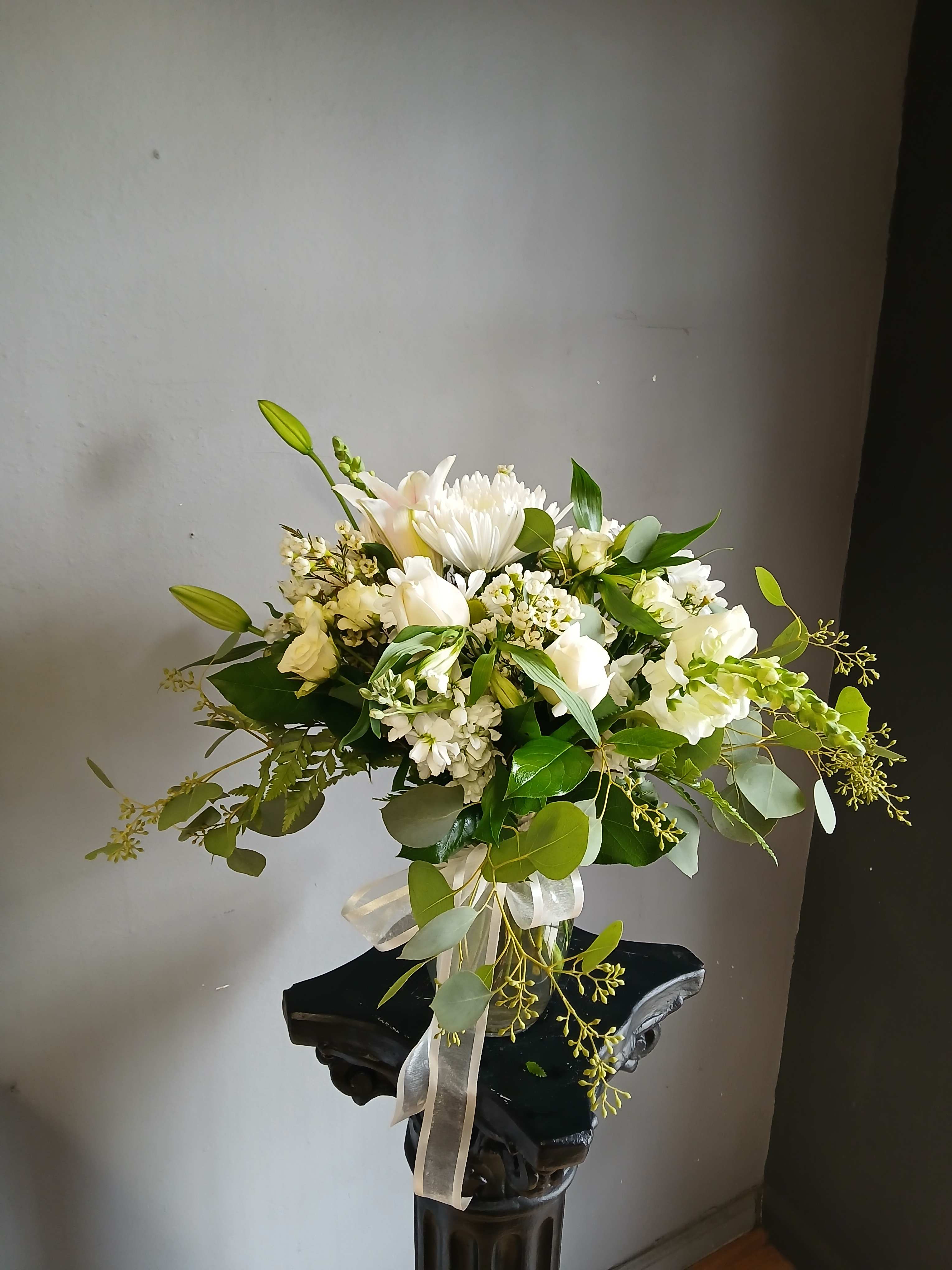 White floral arrangement in a glass vase with a ribbon