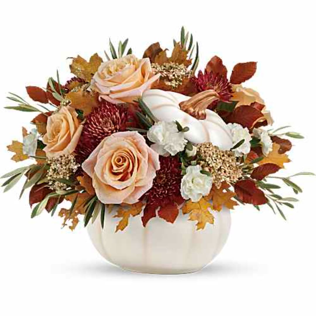 Peach roses and white flowers in a white pumpkin vase with autumn leaves