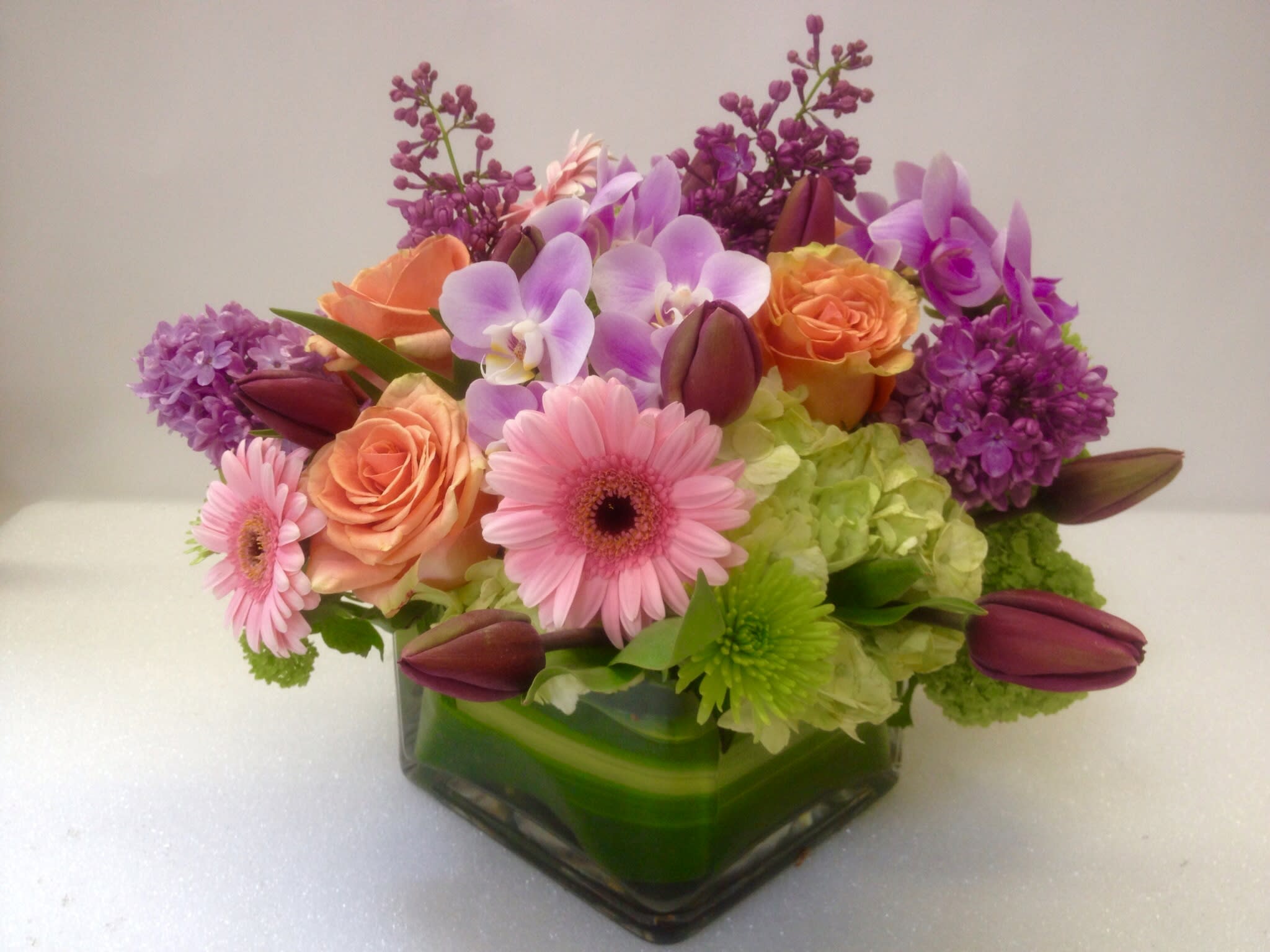 Mixed bouquet in a square glass vase with pink, purple, and orange flowers