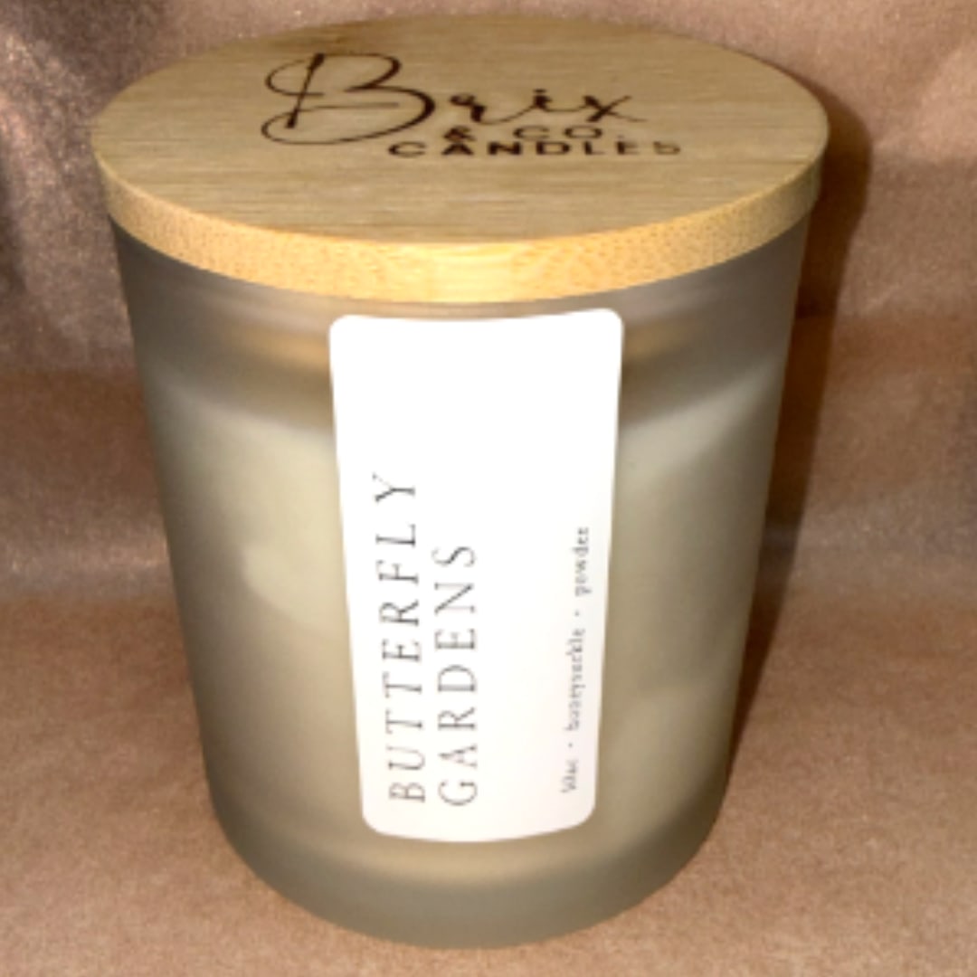 Frosted glass candle jar with a wooden lid labeled Butterfly Gardens