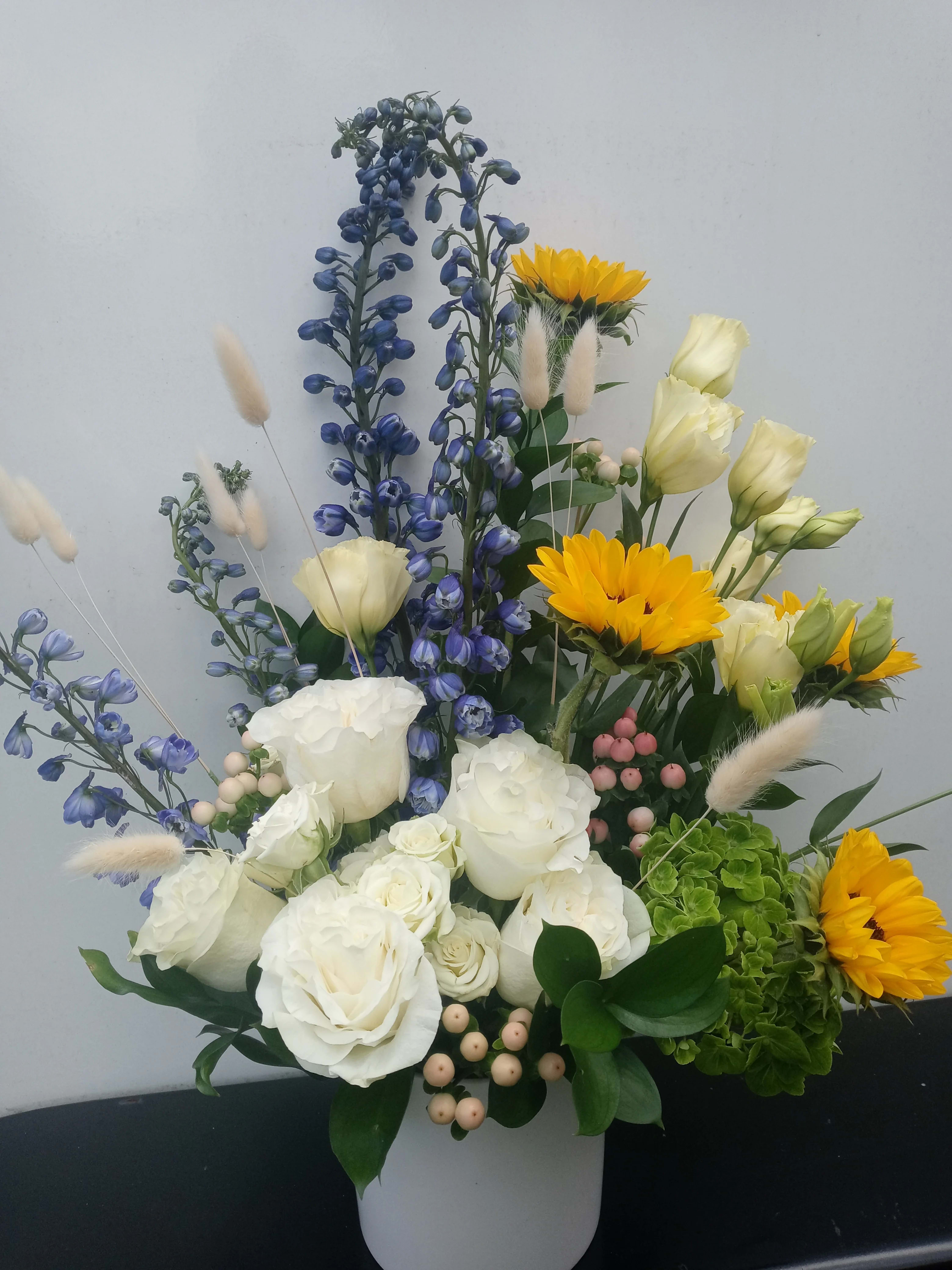 Summer Breeze - Roses, sunflowers, bunny tail grass and more. Designed in a white ceramic container.