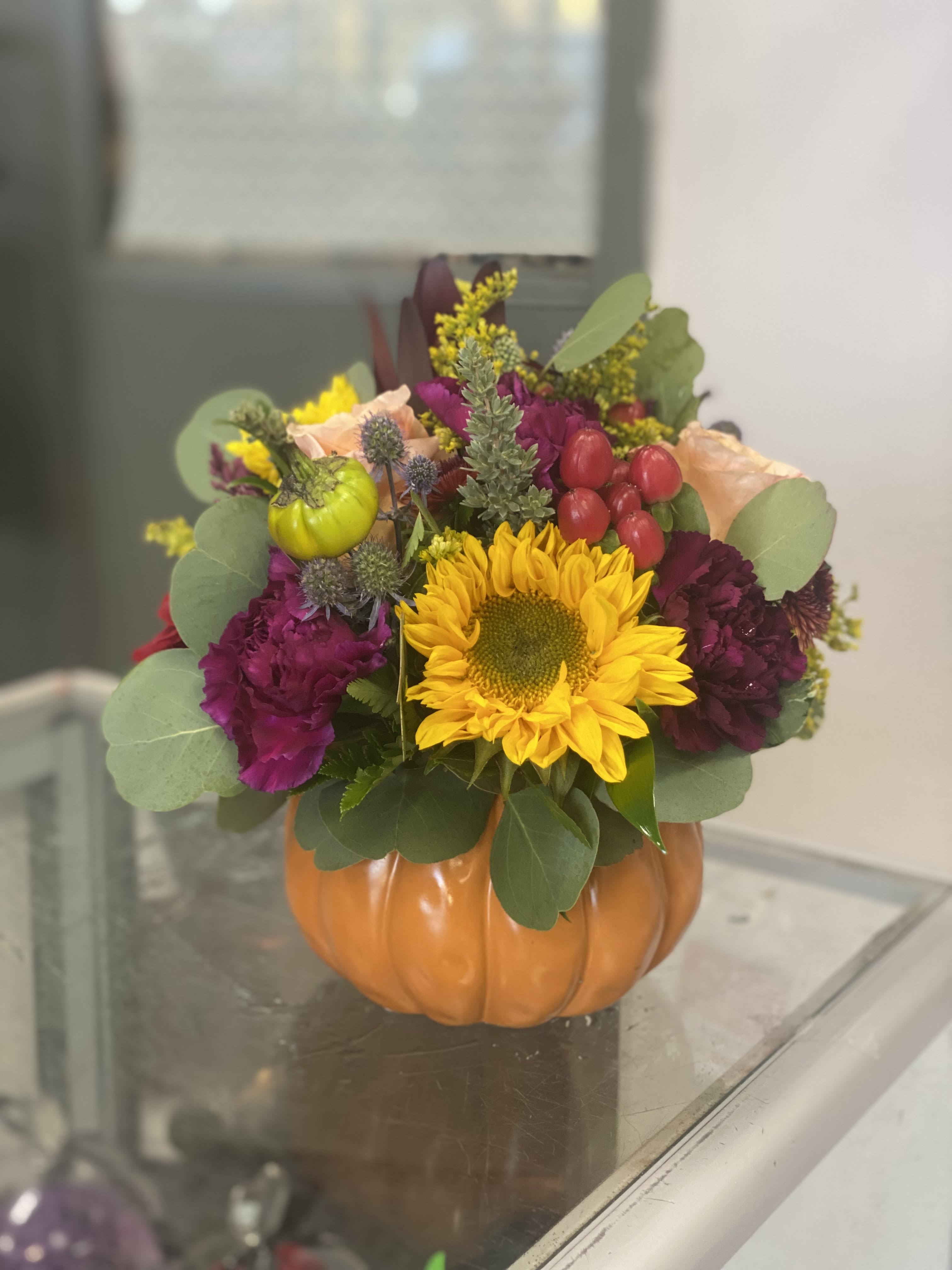 Fall floral arrangement in a pumpkin-shaped container with a sunflower and purple blooms