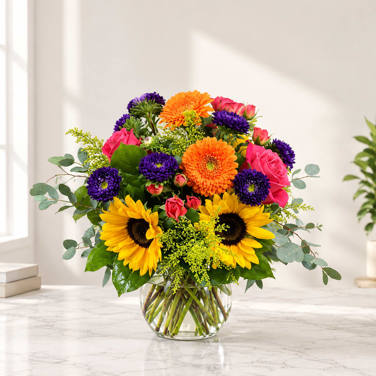 Bright mixed bouquet in a clear glass vase with sunflowers, roses, and purple blooms