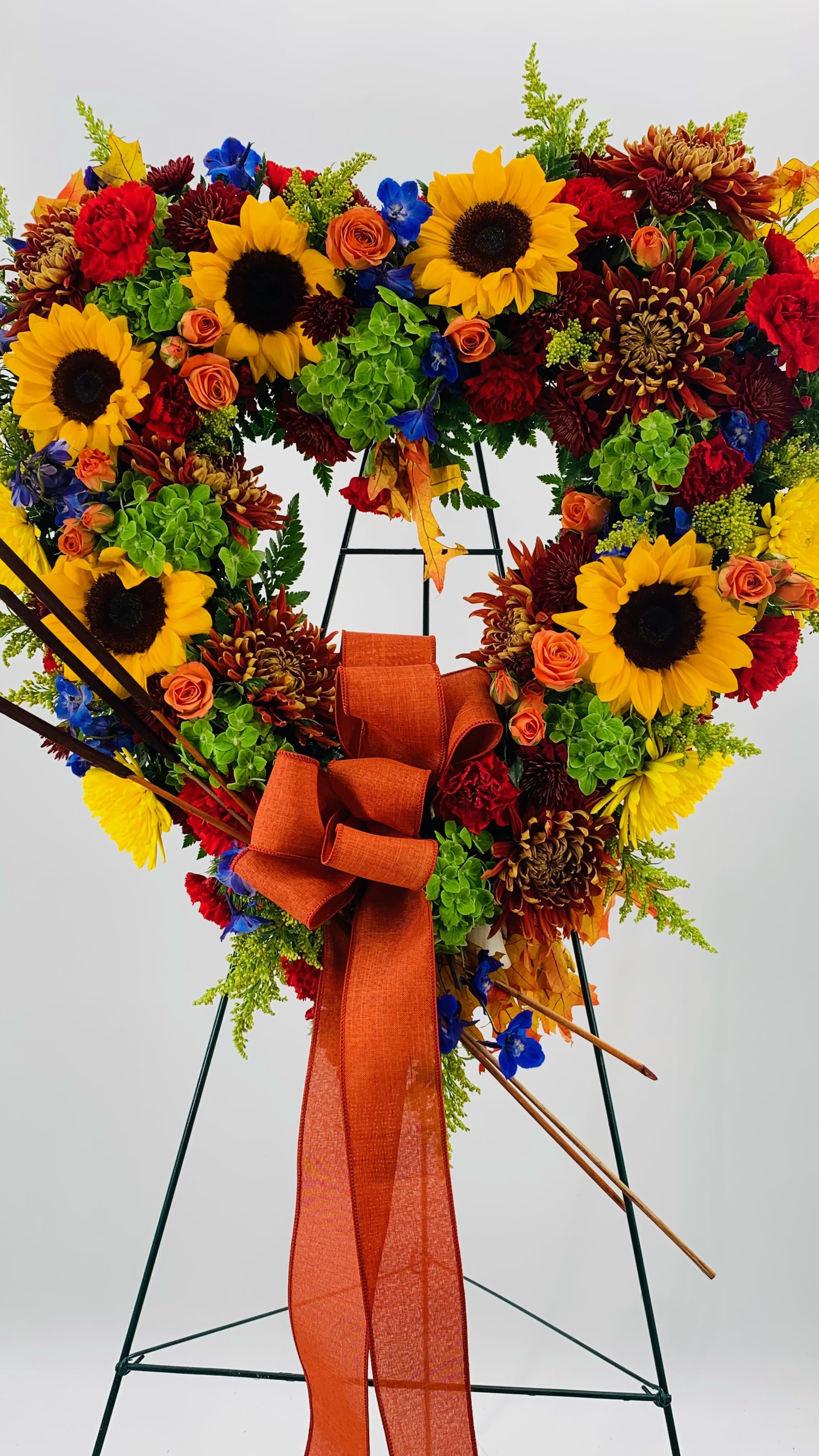 Heart-shaped floral wreath with sunflowers, roses, and an orange ribbon on an easel