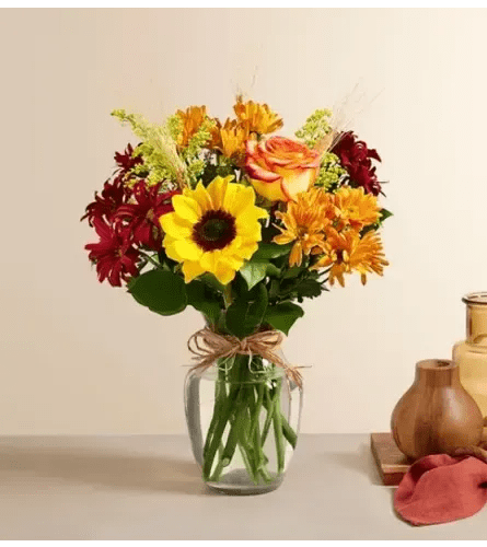 Fallin' 4 fall - Fall arrangment in clear vase that has sunflower(s), red daisies, orange daisies, high magic rose(s), yellow solidago and Sala tips.