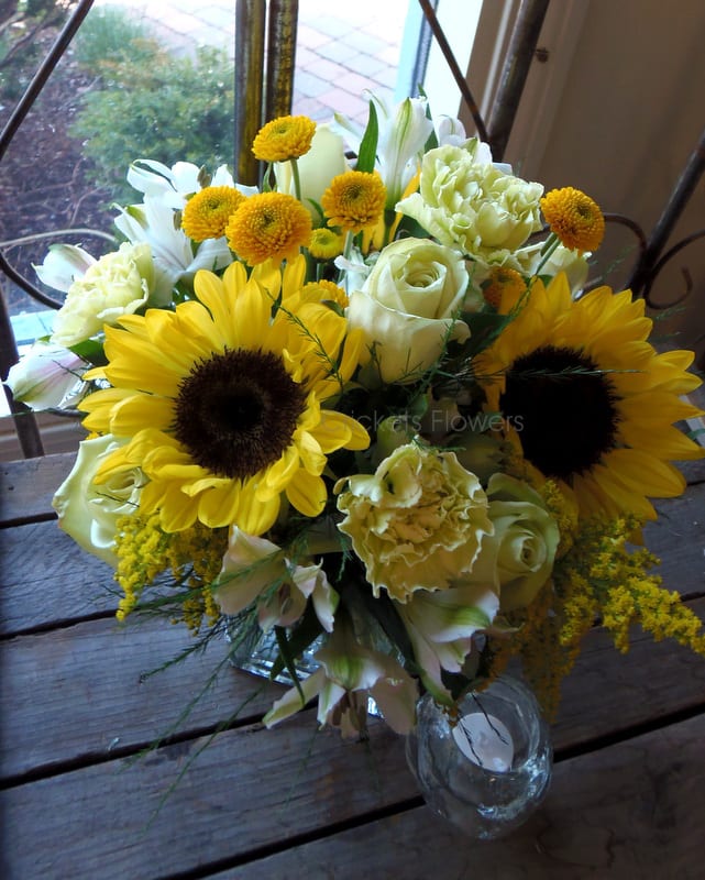 Bouquet of yellow sunflowers, white roses, and lilies in a glass vase
