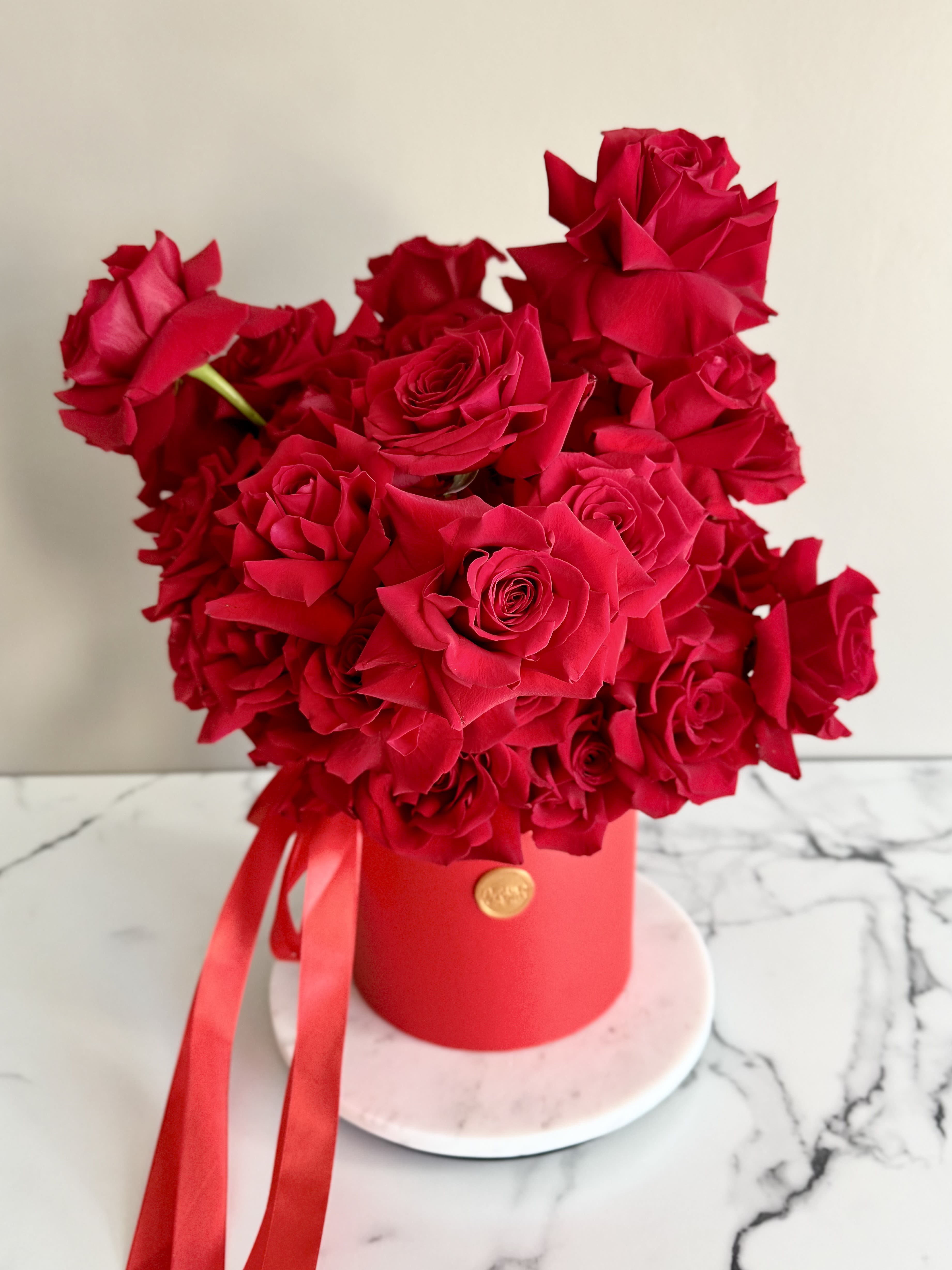 Red roses arranged in a round red box with ribbon