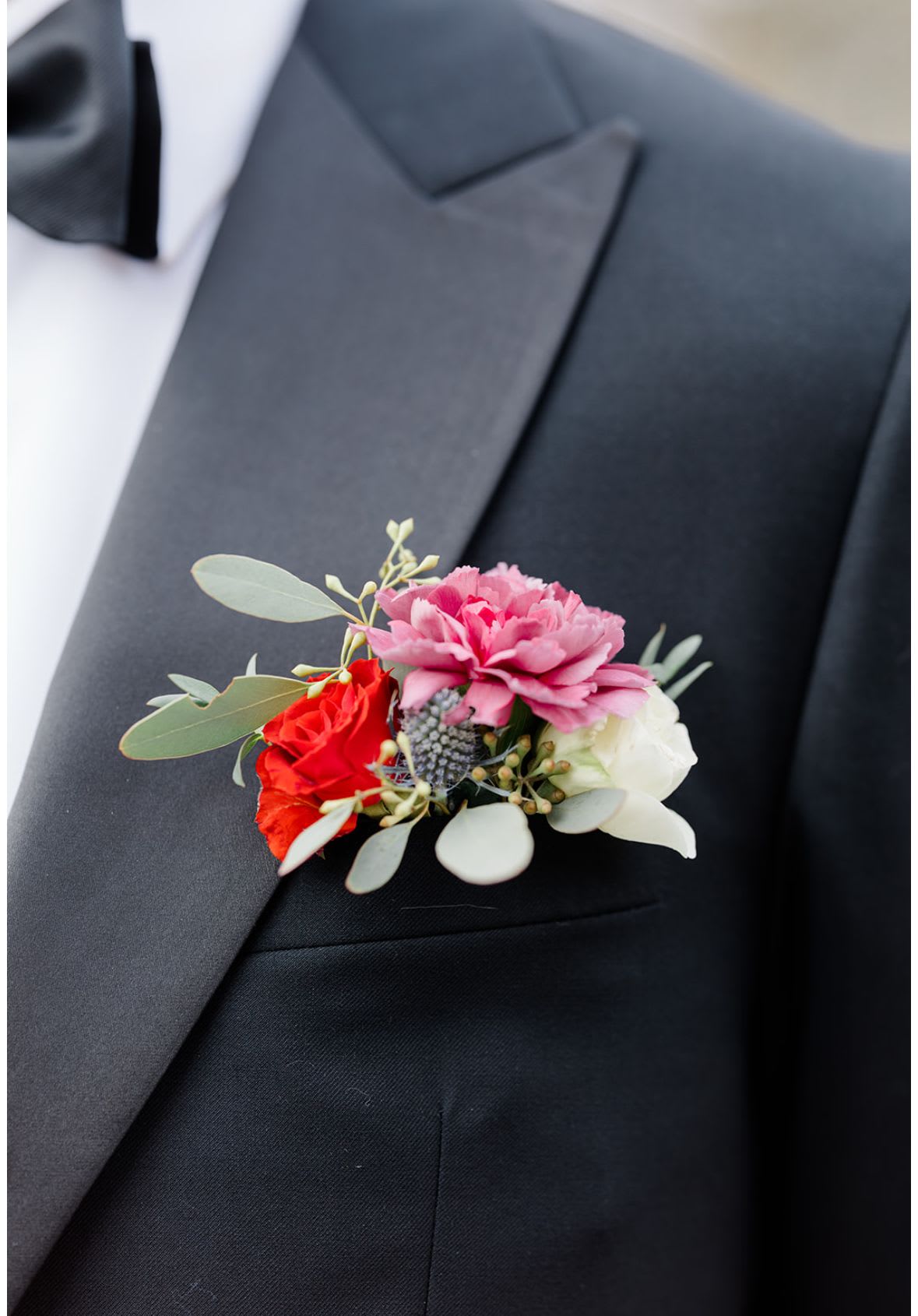 Boutonniere with pink, red, and white flowers on a black suit lapel