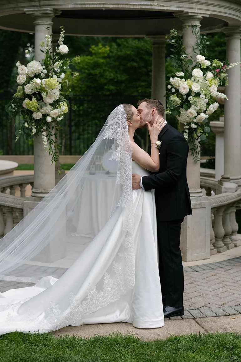 Couple's first kiss with floral pieces on either side of a domed stone area