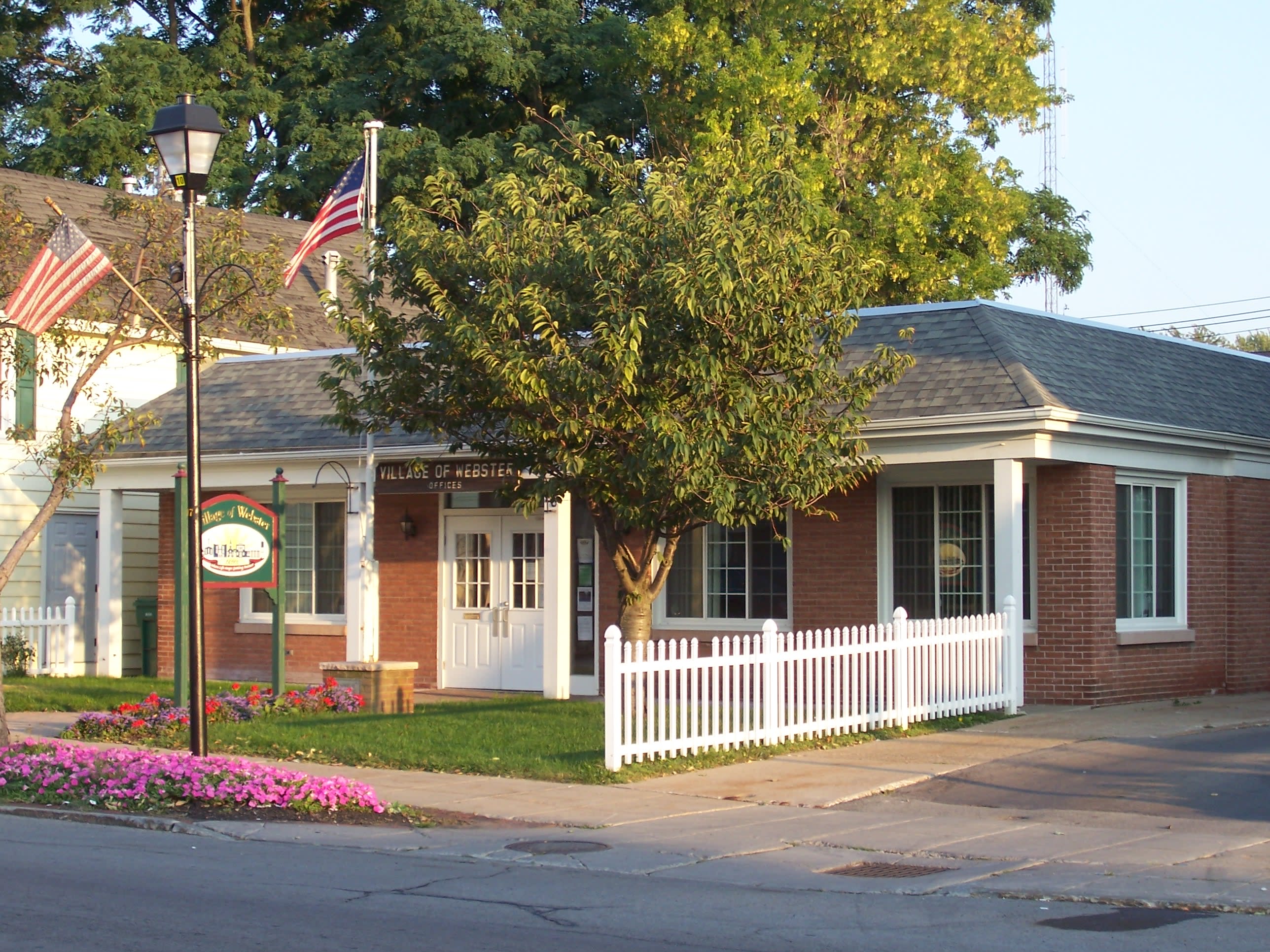 One of Webster's brick town offices complete with a white-picked fence and American flags.