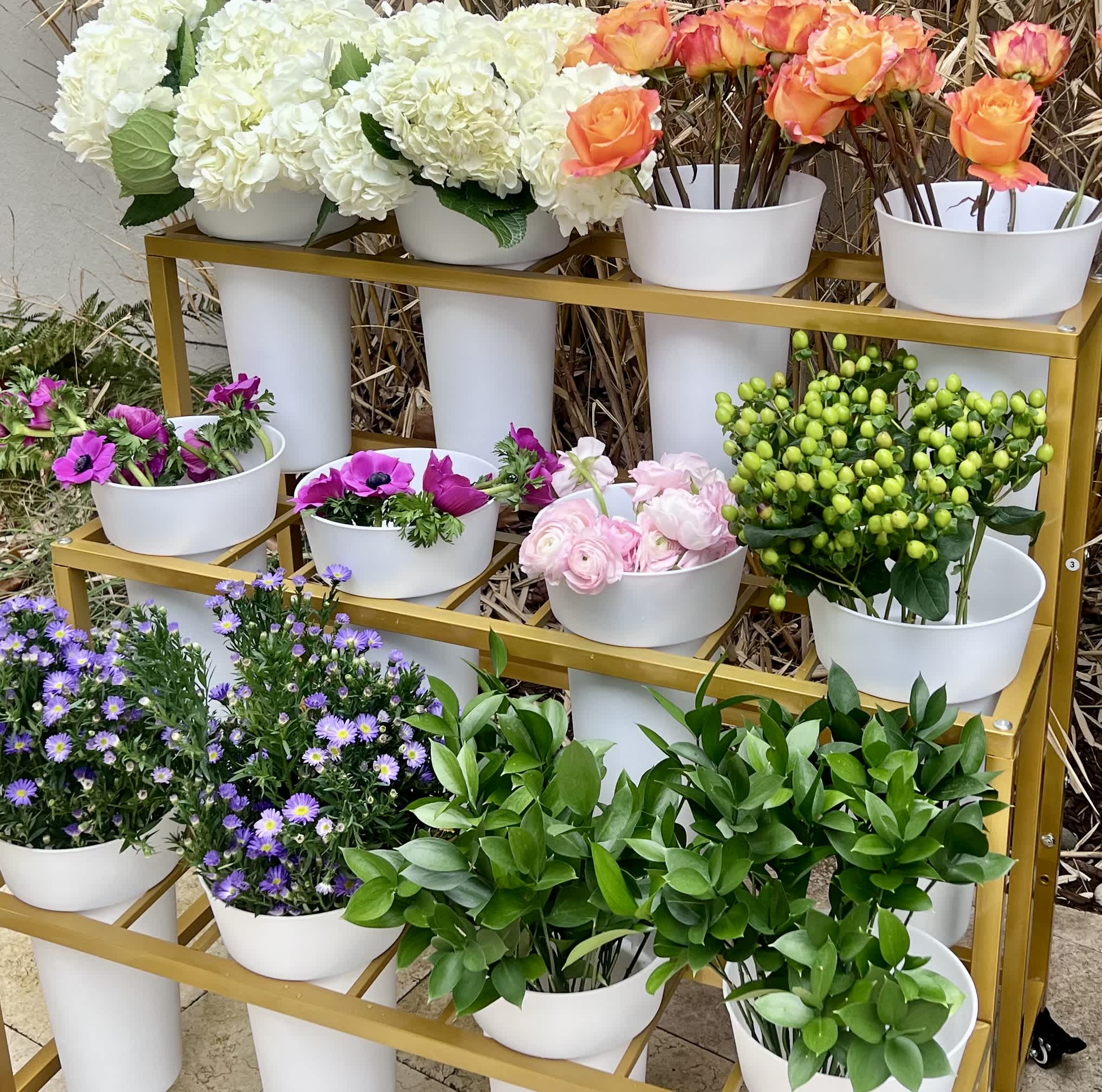 An image of a flower cart with three tiers of white buckets filled with a variety of  flowers. 