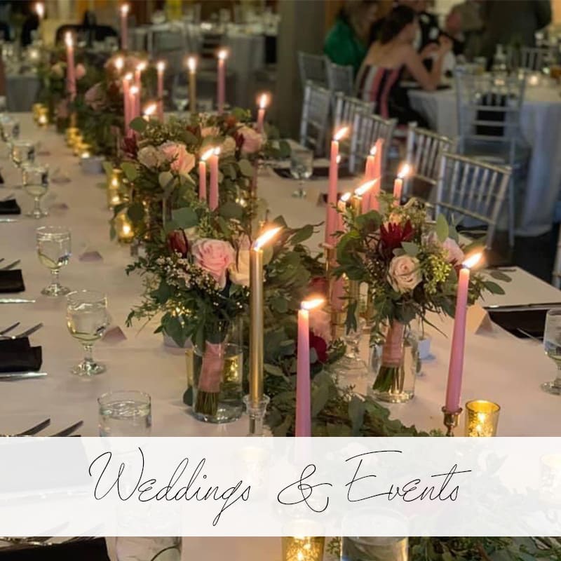 Centerpiece with pink and gold lit cangles and pink roses with greenery with banner that says Wedding and Events