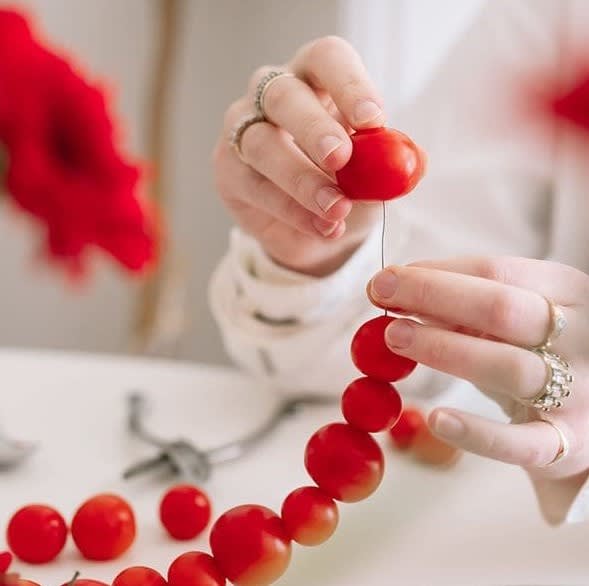 Hands threading tomatoes onto fishing line to create a new element for a Thanksgiving floral design
