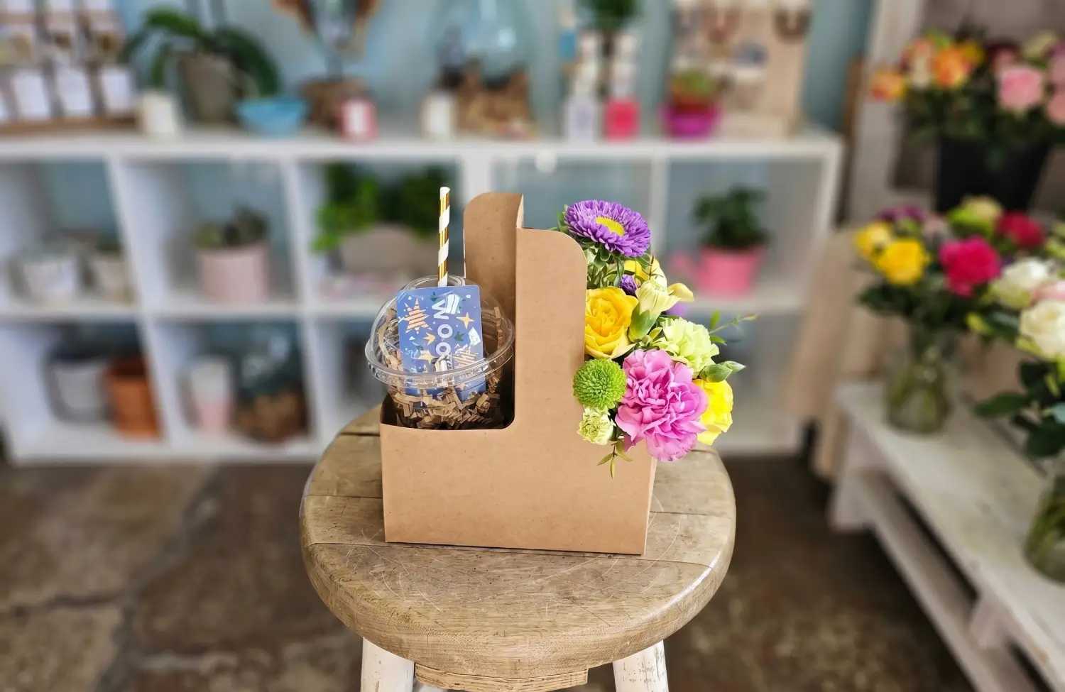 A unique gift combo with a floral arrangement and drink cup on a stool, crafted by a local flower shop near me boutique.