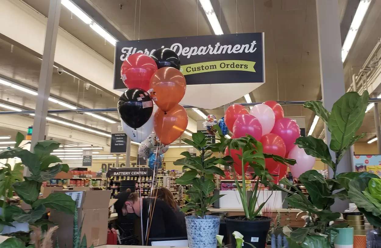 Supermarket floral department with colorful balloons and potted plants, showing a convenient flower shop near me option.