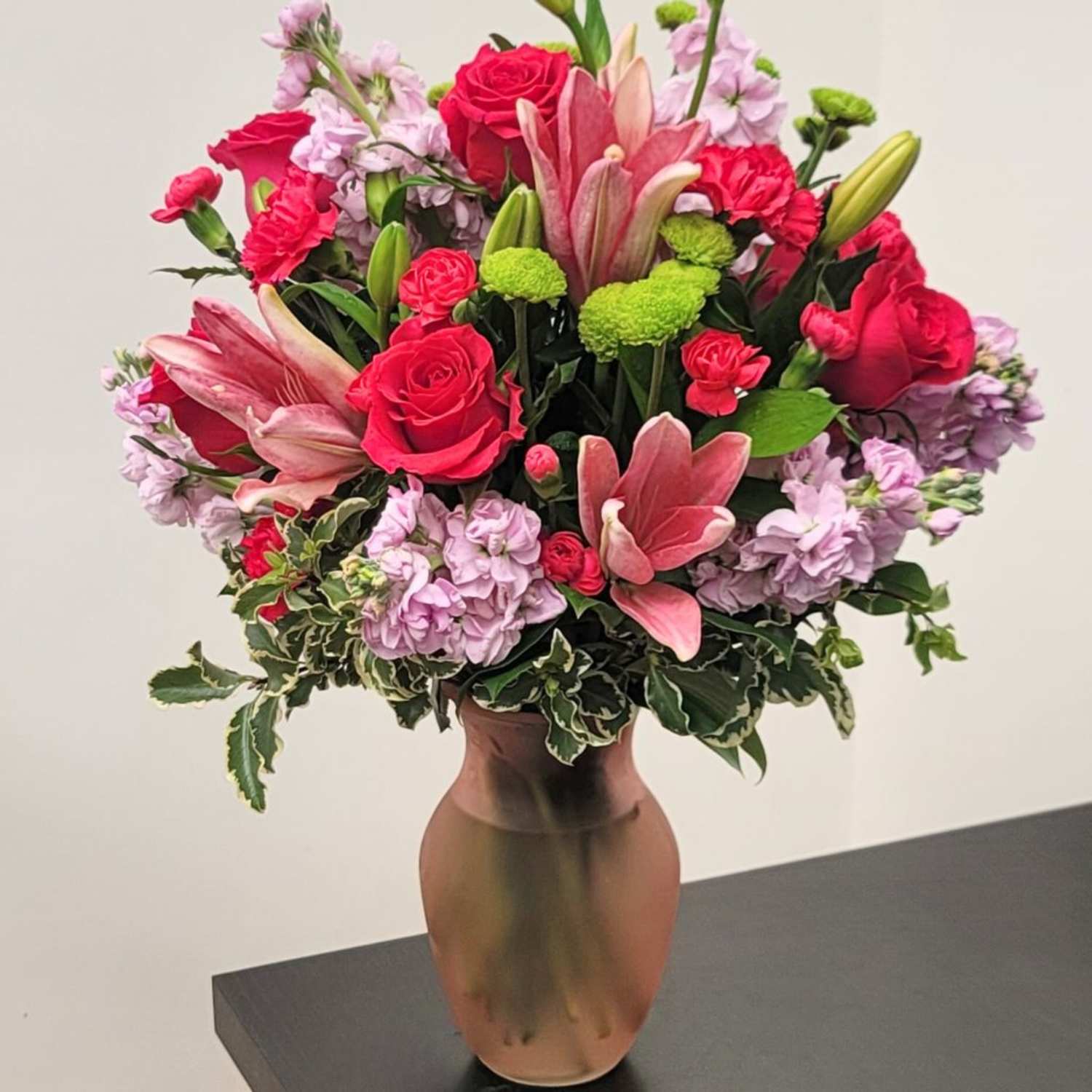Vivid pink and purple arrangement in a frosted pink vase