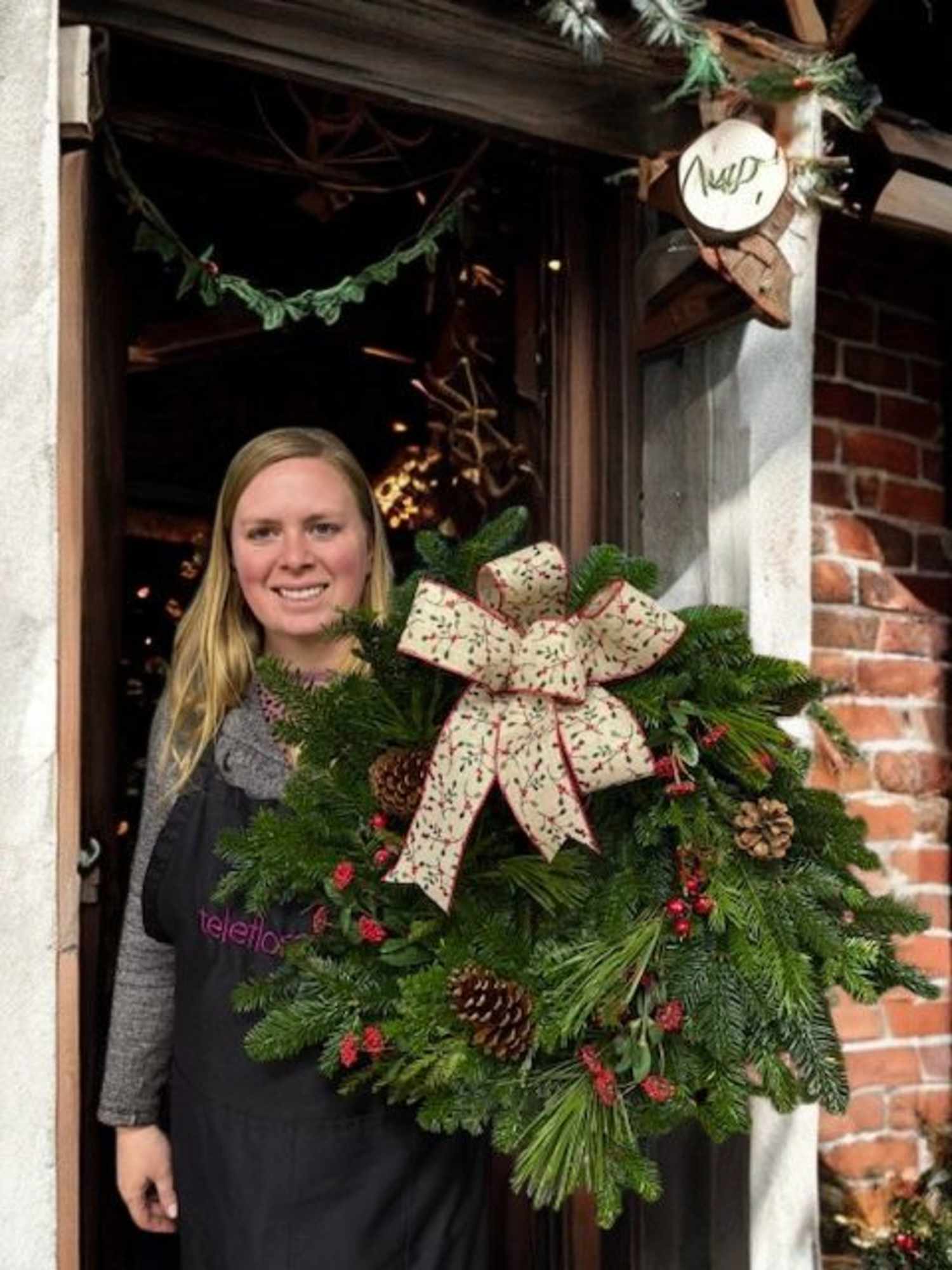 Woman holding wreath with large bow and pine cones