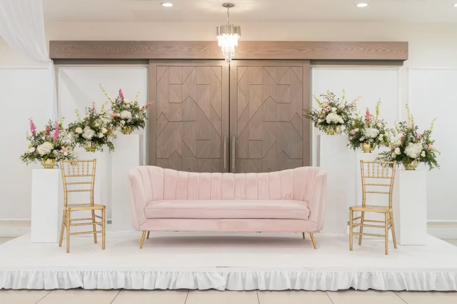 Pink couch bookended by two gold chairs and six floral arrangements on pedestals