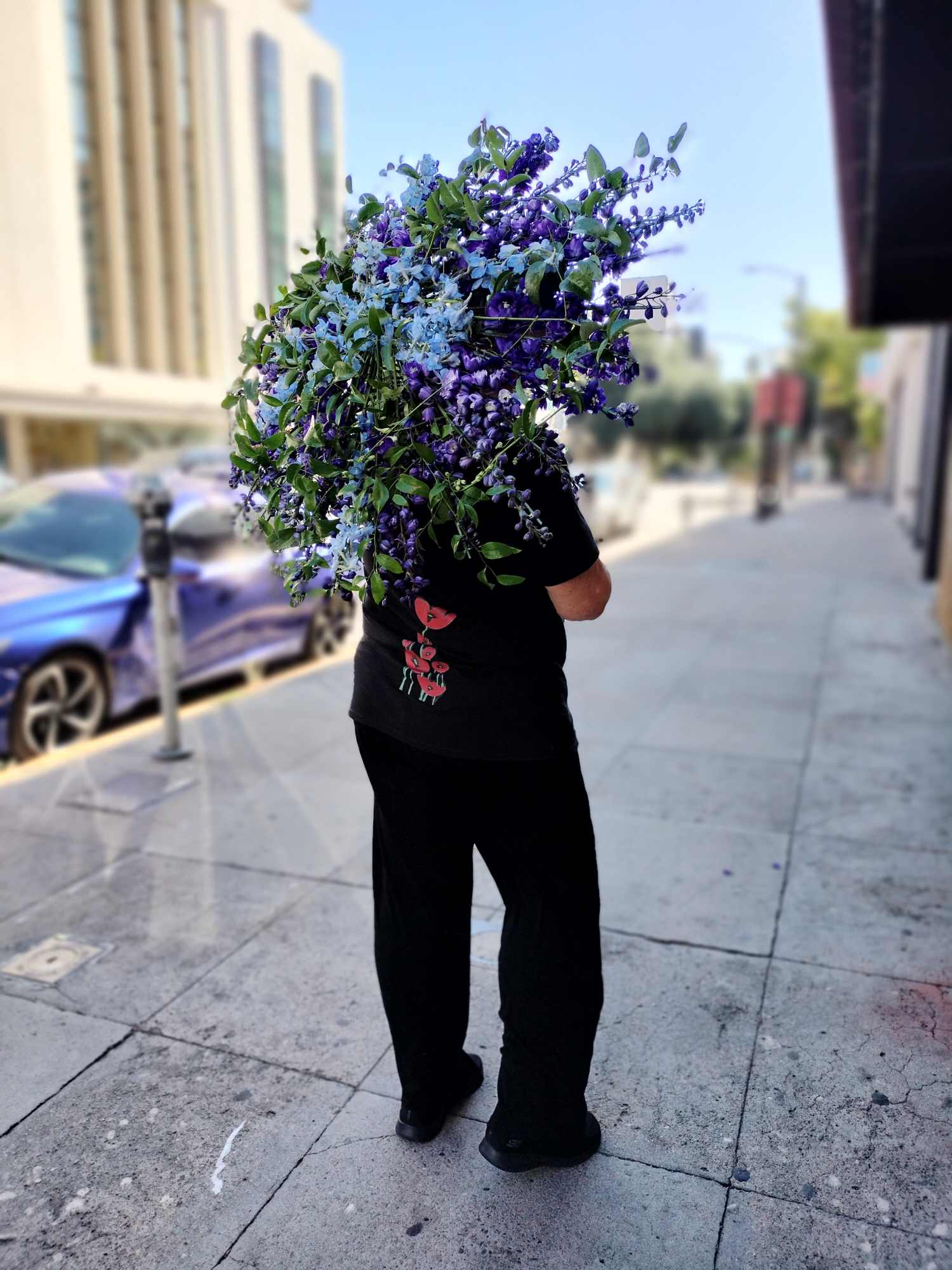 Liezet holding an umbrella made out of blue flowers and greenery  while standing outside of Bloem Decor Florist on 10th street in sacramento californiar