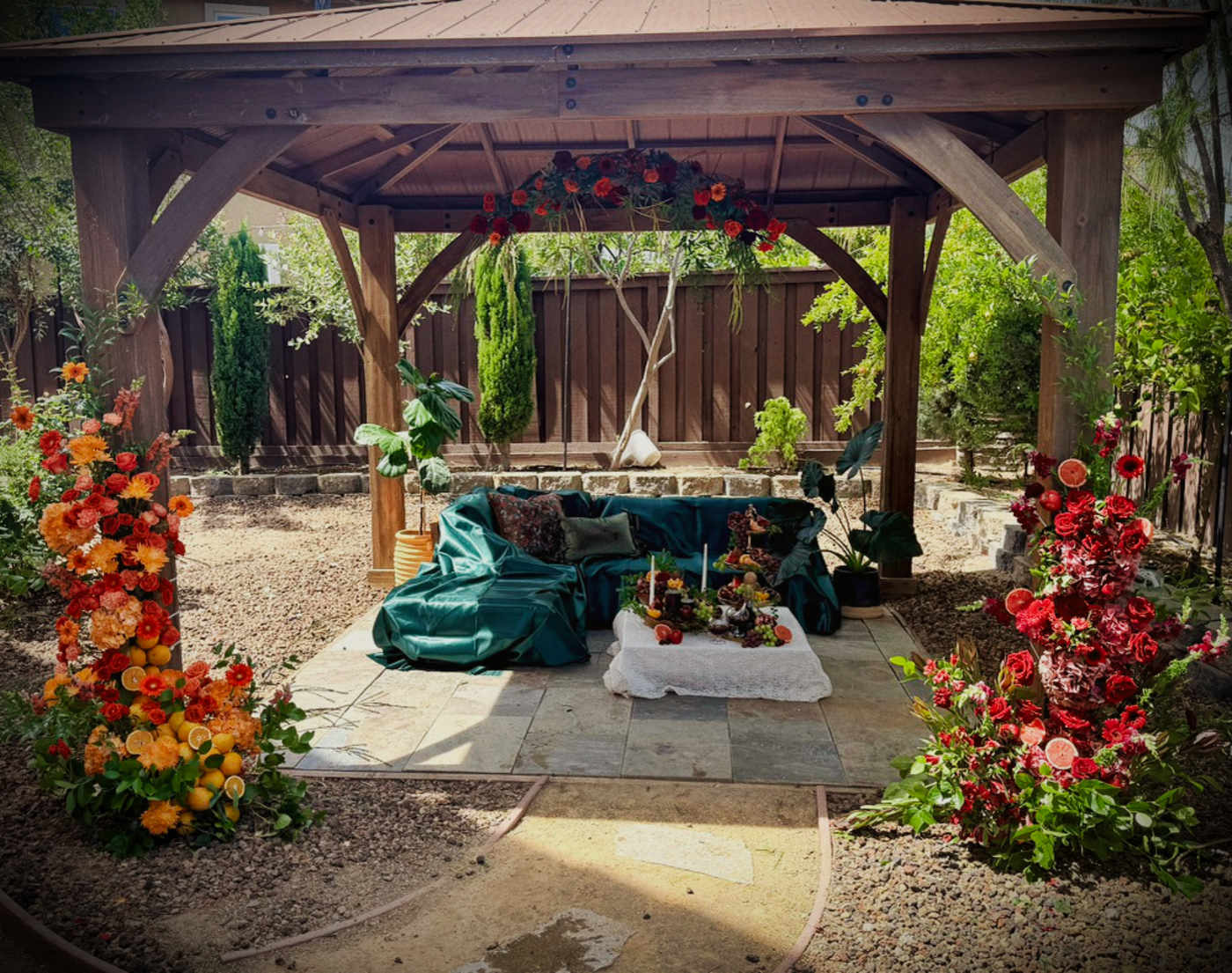 Large orange and red floral installation with roses, gerbera daisies, citrus fruit and greenery surrounding an outdoor lounge.