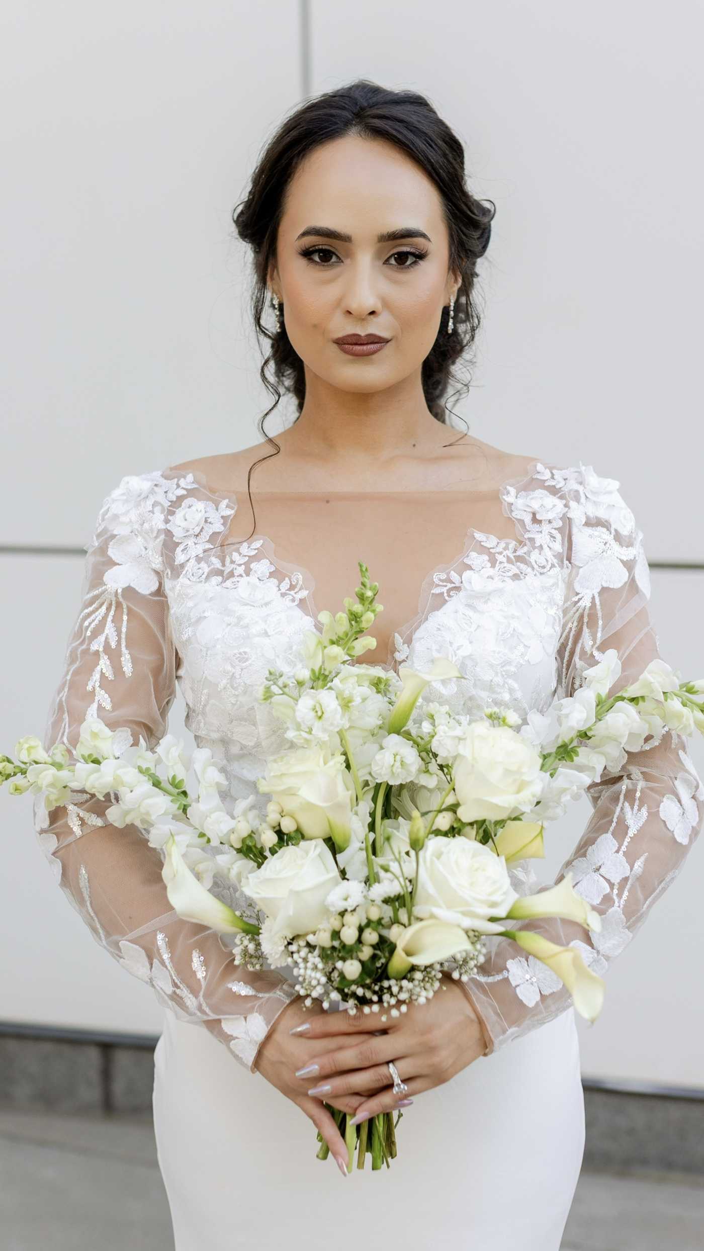 Bride holding an elegant all-white bouquet with roses, calla lilies and delicate white flowers.