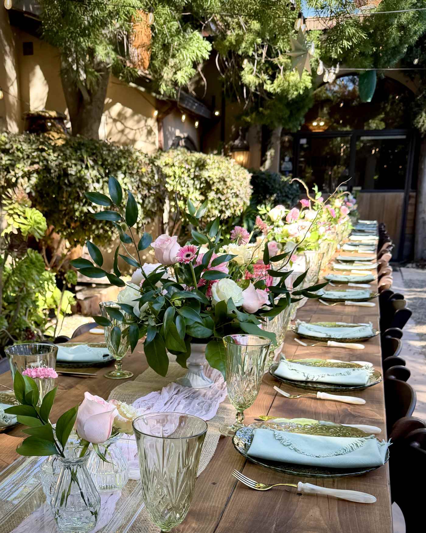 Pink roses and white flowers with greenery arranged along an elegant outdoor wedding reception table.