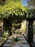 Long outdoor wedding table beneath a greenery-covered arch with pink and ivory floral centerpieces.
