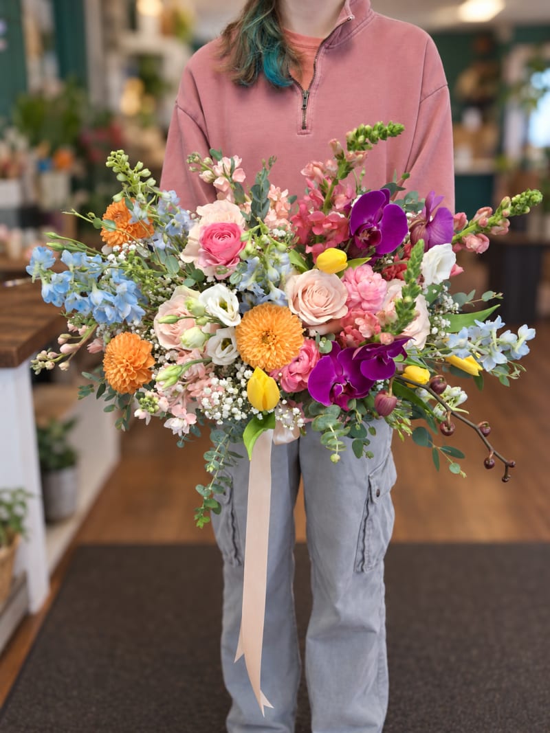 Colorful garden wedding bouquet with pink roses, purple orchids, orange flowers, and blue delphinium.