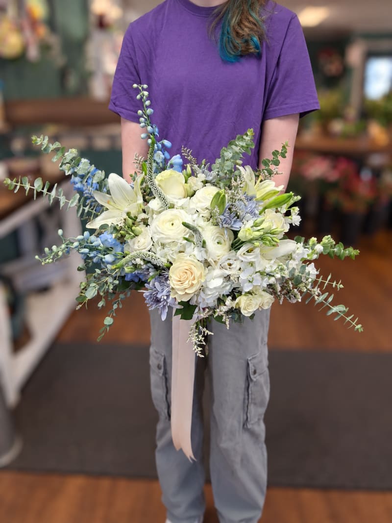 Airy ivory and pale blue wedding bouquet with roses, lilies, delphinium, and eucalyptus.