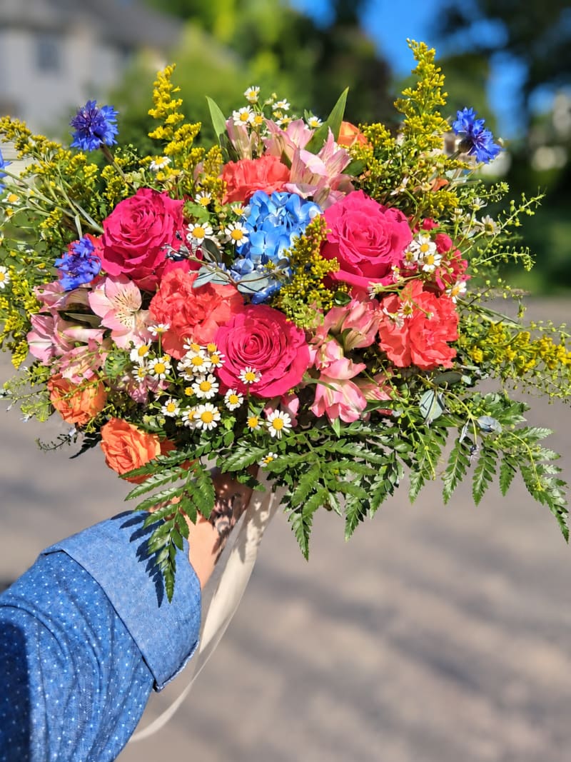 Bright pink and blue bouquet with roses, hydrangea, daisies, and yellow wildflower accents.