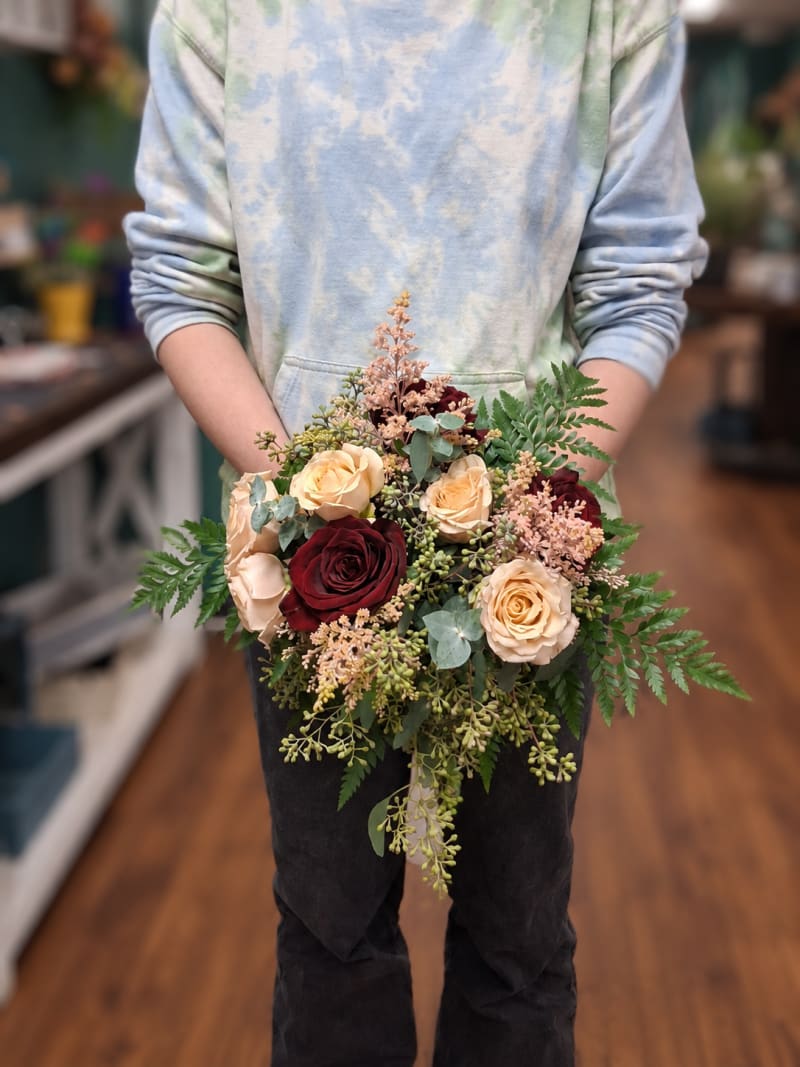 Burgundy and peach rose wedding bouquet with eucalyptus, fern, and blush accents.