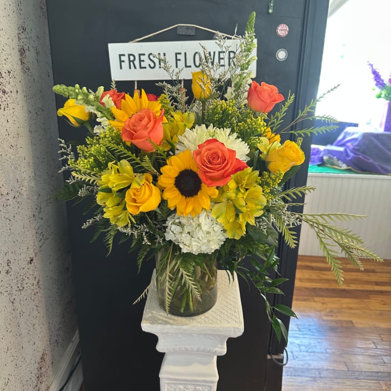 Yellow sunflowers, orange roses, and white blooms in a vase.