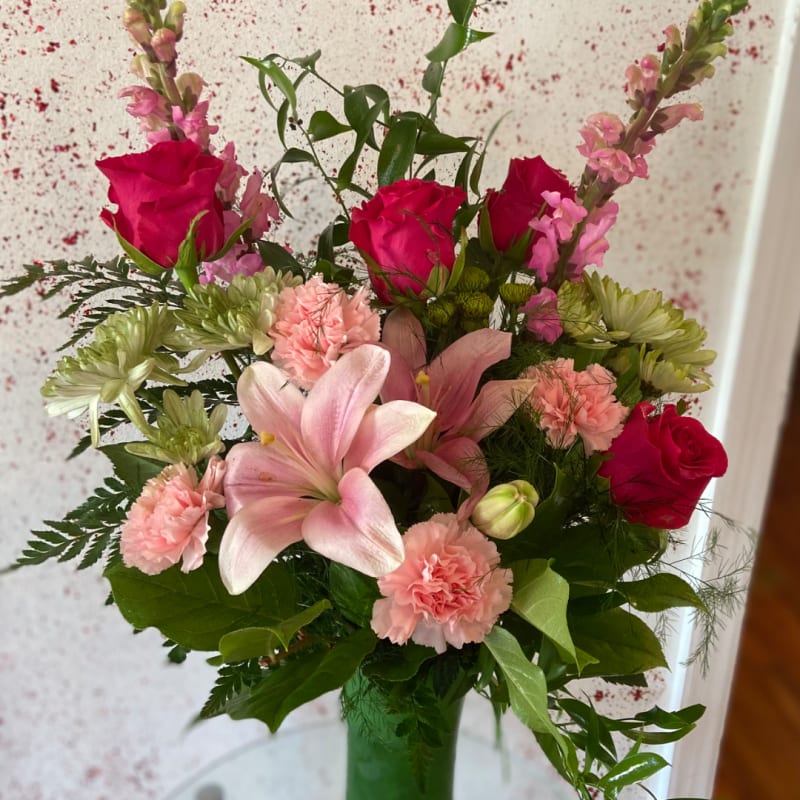 Red roses, pink lilies, and fresh greenery in a vase.