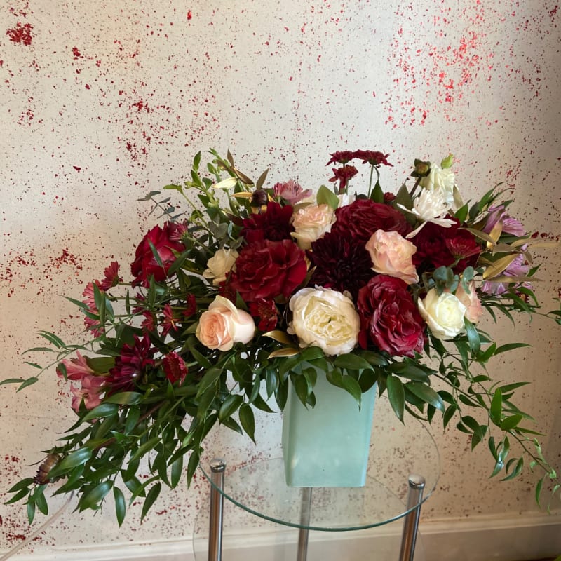 Mixed roses and lush greenery arranged in a pale blue vase.