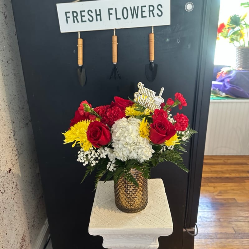 Red roses, white hydrangeas, and yellow blooms in a gold vase.