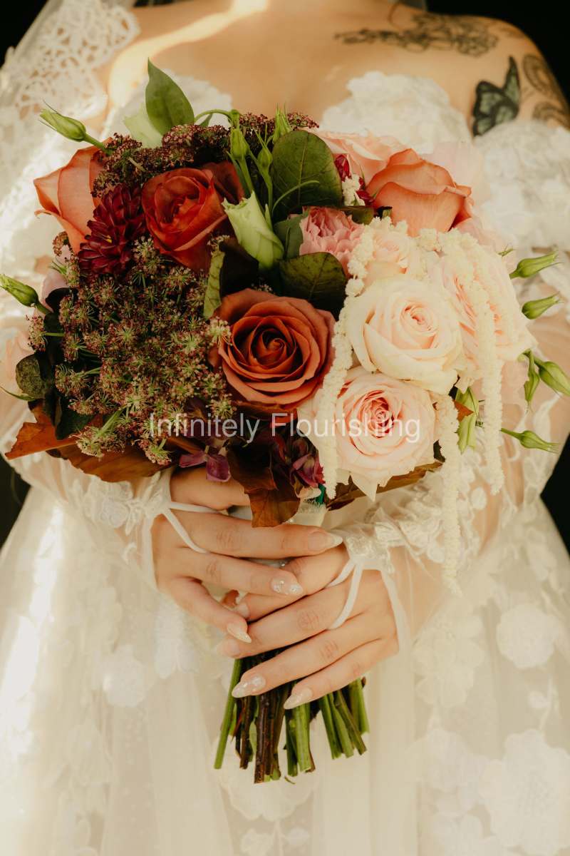 Featuring warm barista roses, blush roses, light pink lisianthus, raspberry hydrangea, copper beech leaves, preserved white hanging amaranthus, and chocolate Queen Anne's lace, this bouquet creates a beautiful balance of romance, depth, and seasonal charm
