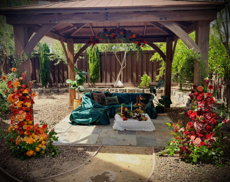 Large orange and red floral installation with roses, gerbera daisies, citrus fruit and greenery surrounding an outdoor lounge.