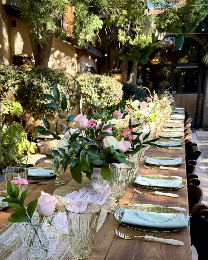 Pink roses and white flowers with greenery arranged along an elegant outdoor wedding reception table.