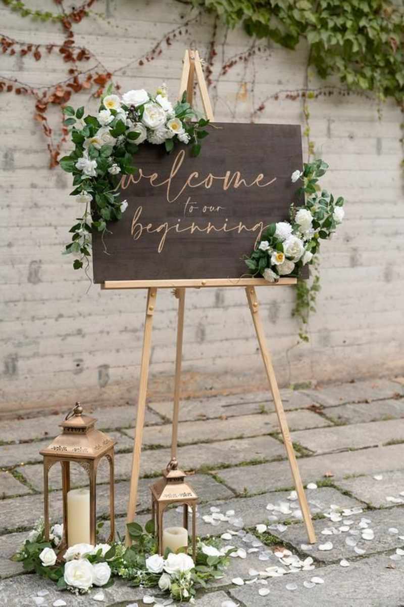 Wedding welcome sign decorated with white flowers and greenery.