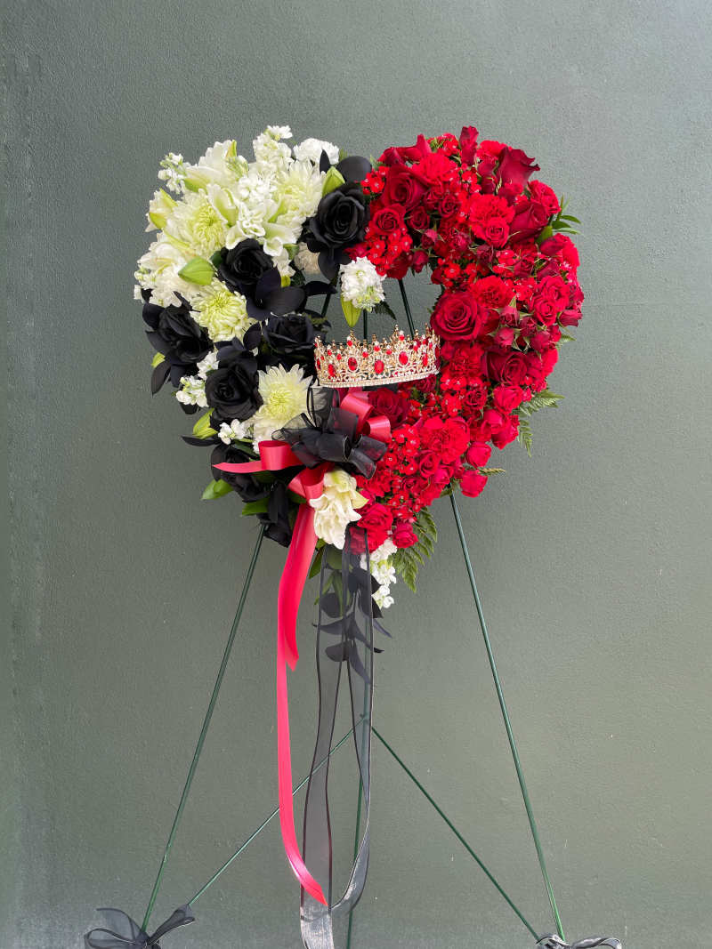 Custom heart-shaped funeral standing spray in premium red and white flowers with a regal crown accent on an easel by Dolly's Florist Miami.