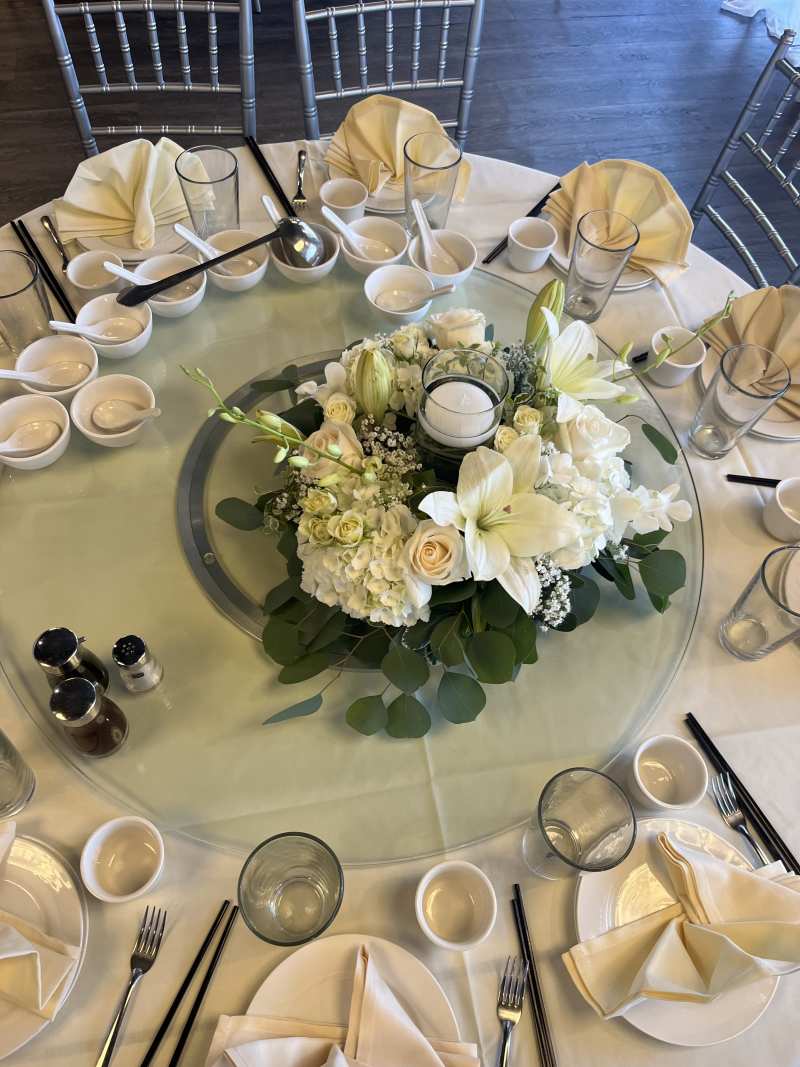 Close-up of a round white floral centerpiece with roses and hydrangeas on a wedding reception table with floating candle.