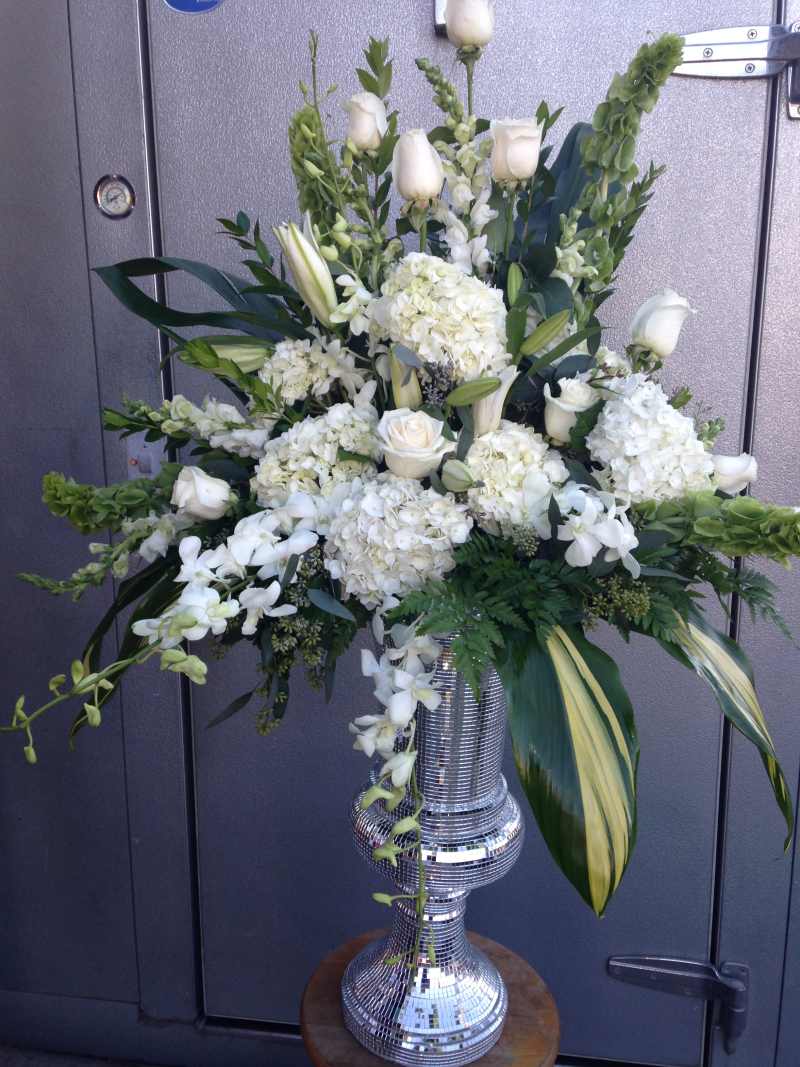 White altar floral arrangement with roses, hydrangeas, orchids, and greenery in an elegant silver vase.
