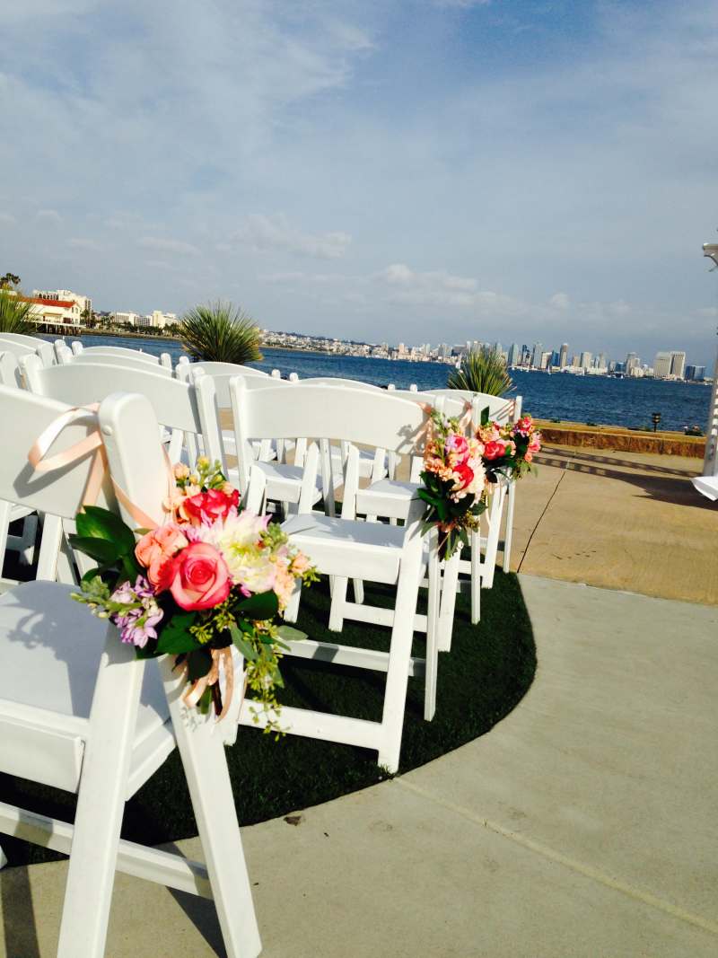 Outdoor wedding ceremony setup with white chairs, bright floral chair arrangements, and bay views at Admiral Kidd Catering and Conference Center on Naval Base Point Loma in San Diego.