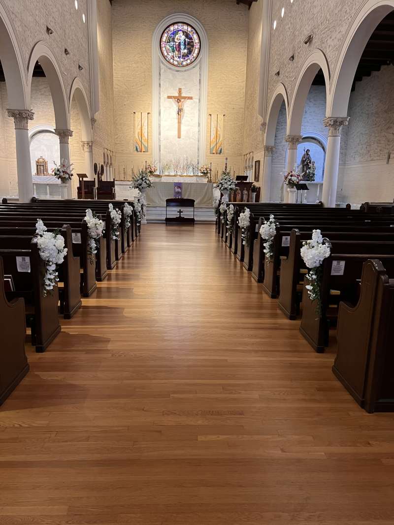 Church wedding ceremony setup with white floral pew markers and altar arrangements at St. Joseph Cathedral in San Diego.