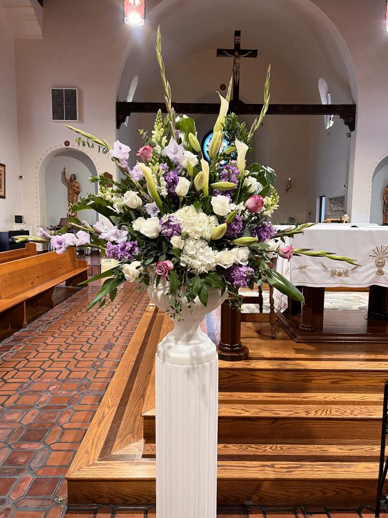 Elevated altar arrangement in a white urn featuring white hydrangeas, roses, calla lilies, lavender blooms, and soft pink flowers at St. Patrick Catholic Parish in North Park, San Diego.
