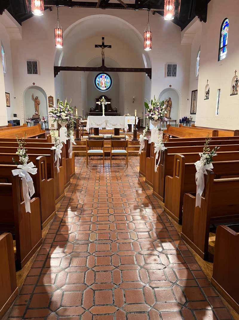 Catholic church wedding ceremony setup with floral aisle markers and altar arrangements at St. Patrick Catholic Parish in North Park, San Diego.