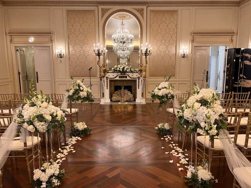 Indoor wedding ceremony with white floral aisle arrangements and rose petals in the Versailles Room at The Westgate Hotel.