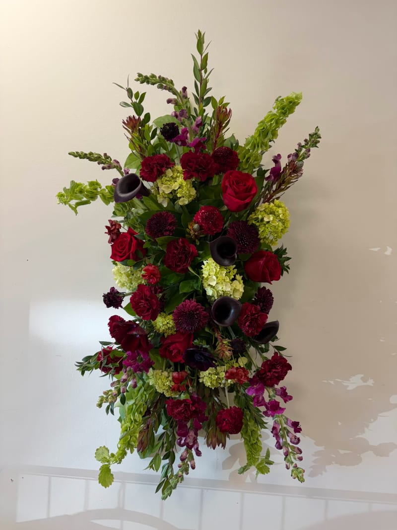 a standing Spray arrangement in shades of deep red, purple, and natural greens