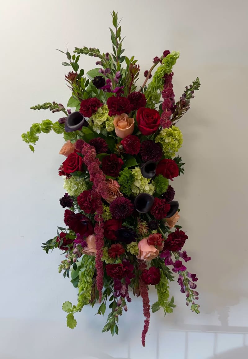 a standing spray arrangement in shades of deep red, purple, and natural green